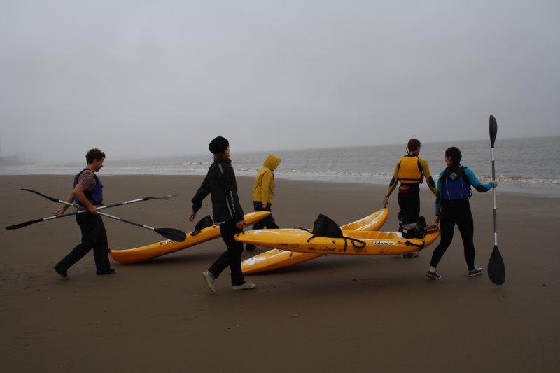 People carrying kayaks towards the beach